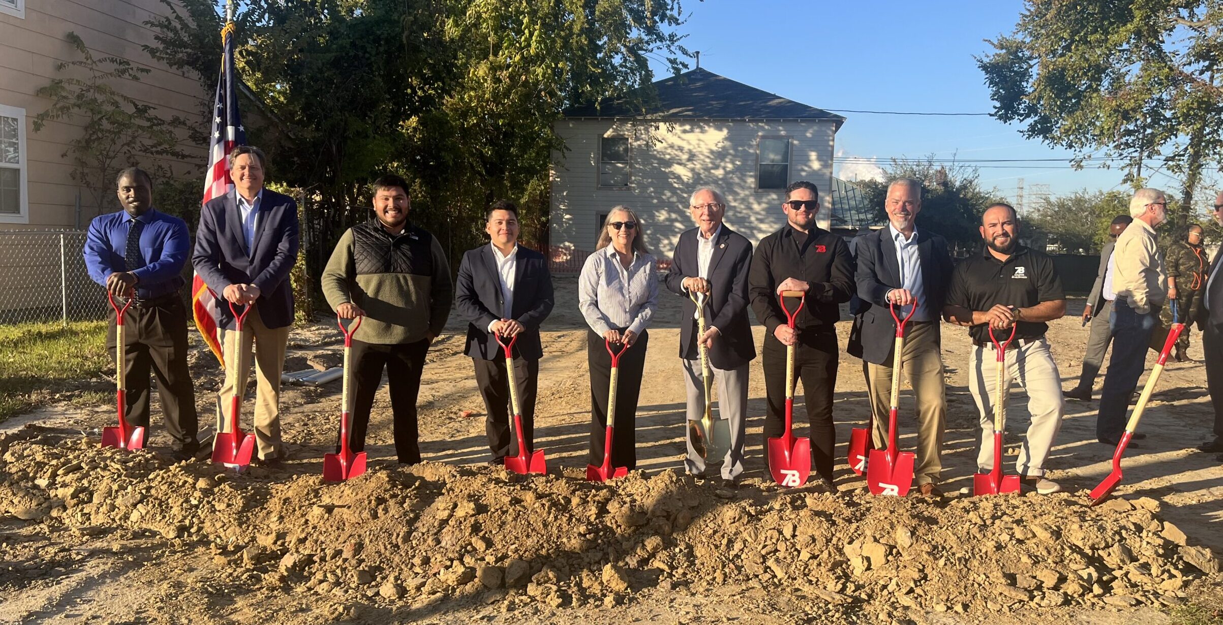 Group of people posing with shovels behind dirt